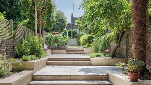 A set of concrete steps leading up to a building entrance, surrounded by greenery and a brick wall. - Historic, elegant and luxurious home in St John's Wood, central London (London)
