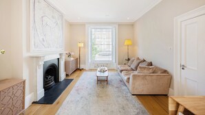 A living room with a fireplace, a sofa, a coffee table, and a large window. - Historic, elegant and luxurious home in St John's Wood, central London (London)