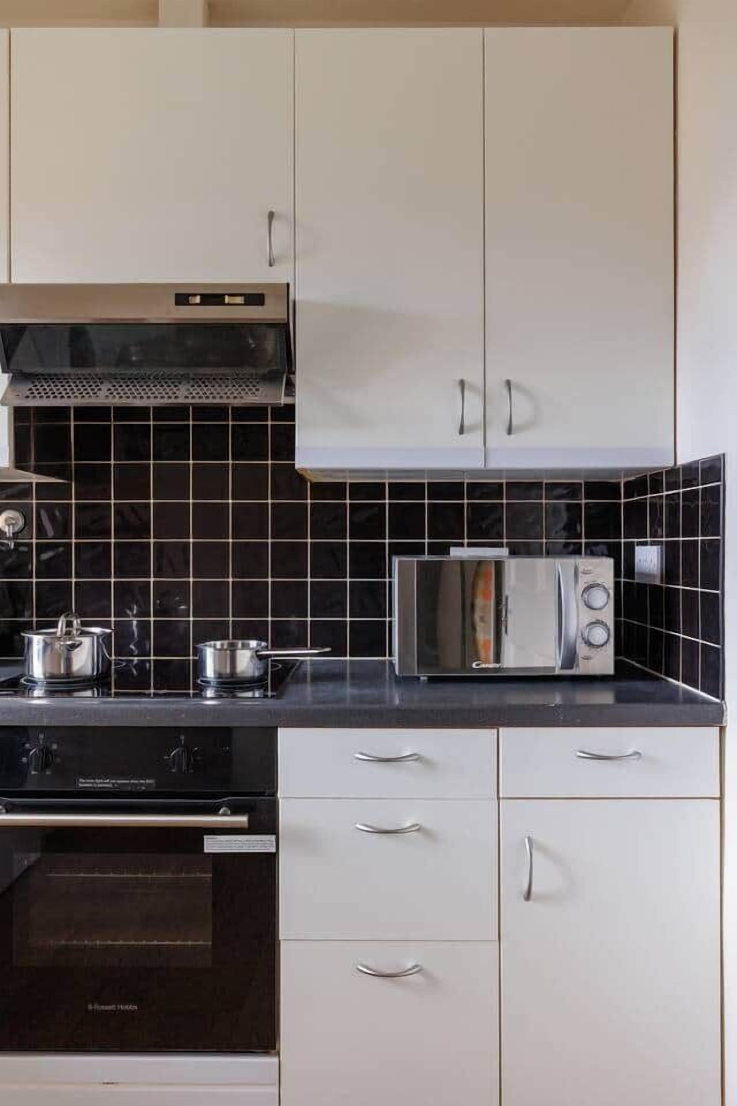 Une cuisine équipée d’un four à micro-ondes, d’une cuisinière et d’un four traditionnel. On y trouve des placards avec des poignées et un pare-feu en carreaux.