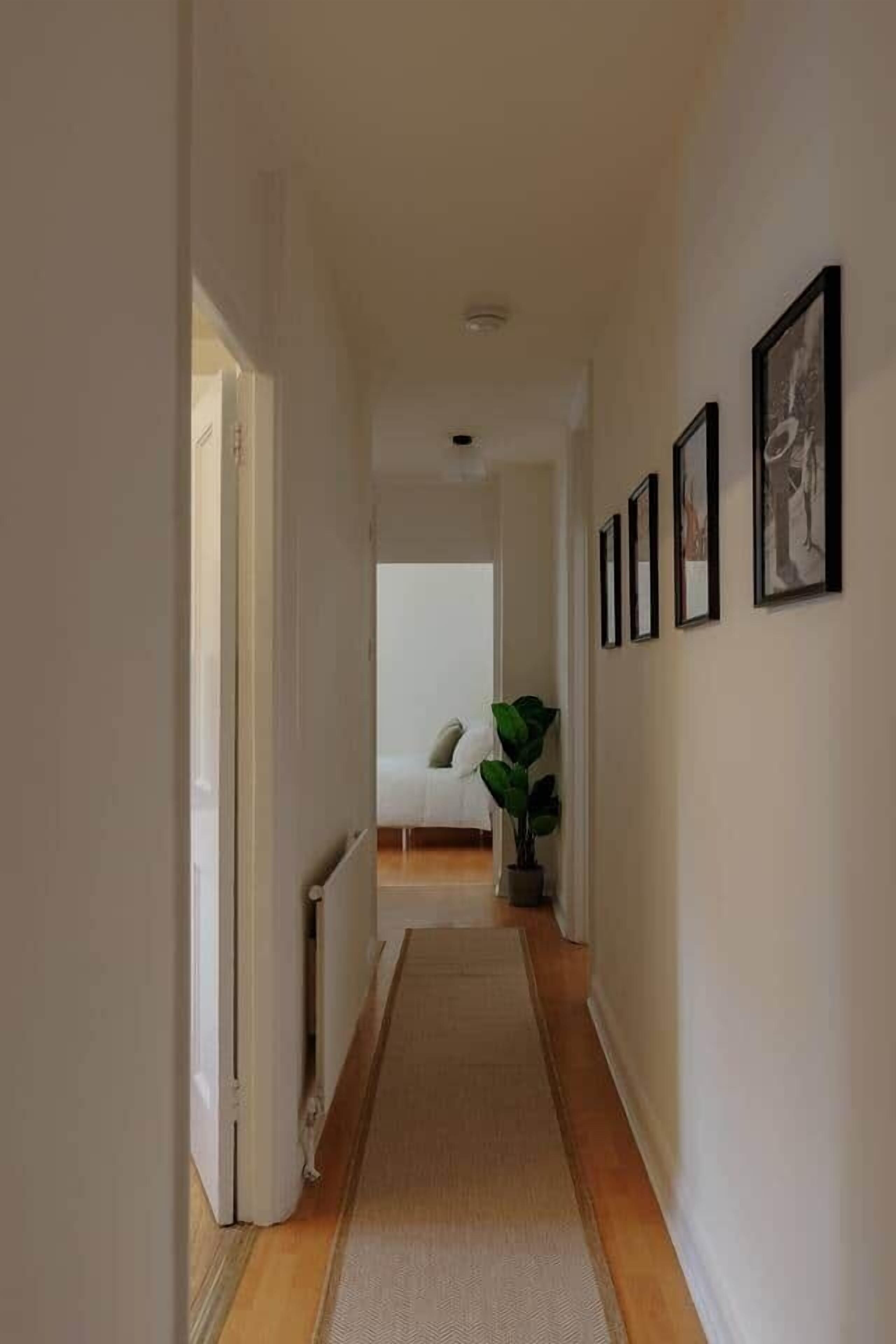 A narrow hallway with a carpet, a radiator, and framed pictures on the wall.