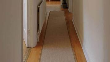 A narrow hallway with a carpet, a radiator, and framed pictures on the wall.