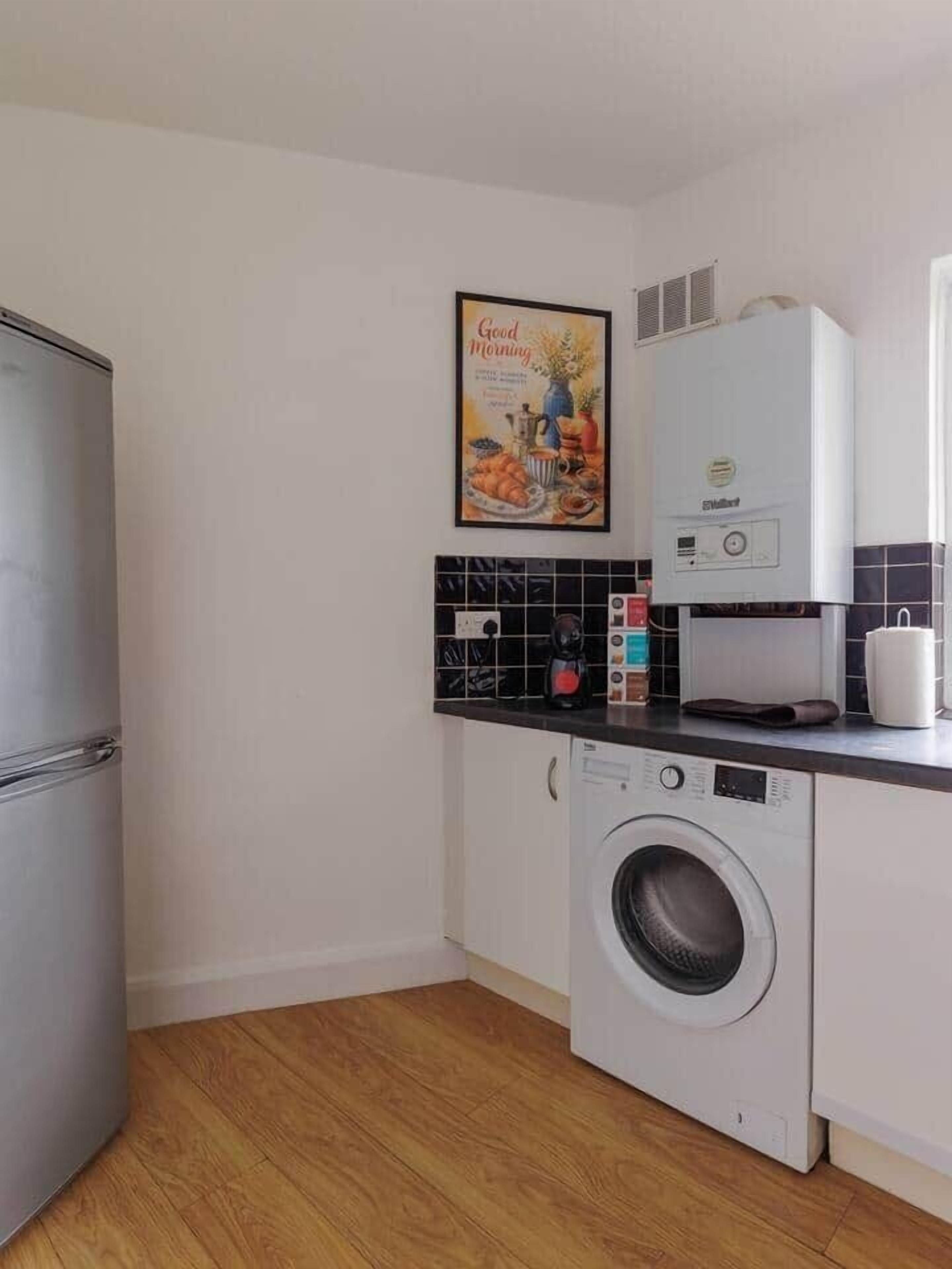 Une cuisine compacte équipée d’un lave-linge, d’une machine à café et d’un réfrigérateur.