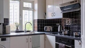 Una cocina con armarios blancos, salpicadero de baldosas negras, una ventana y una lavadora.