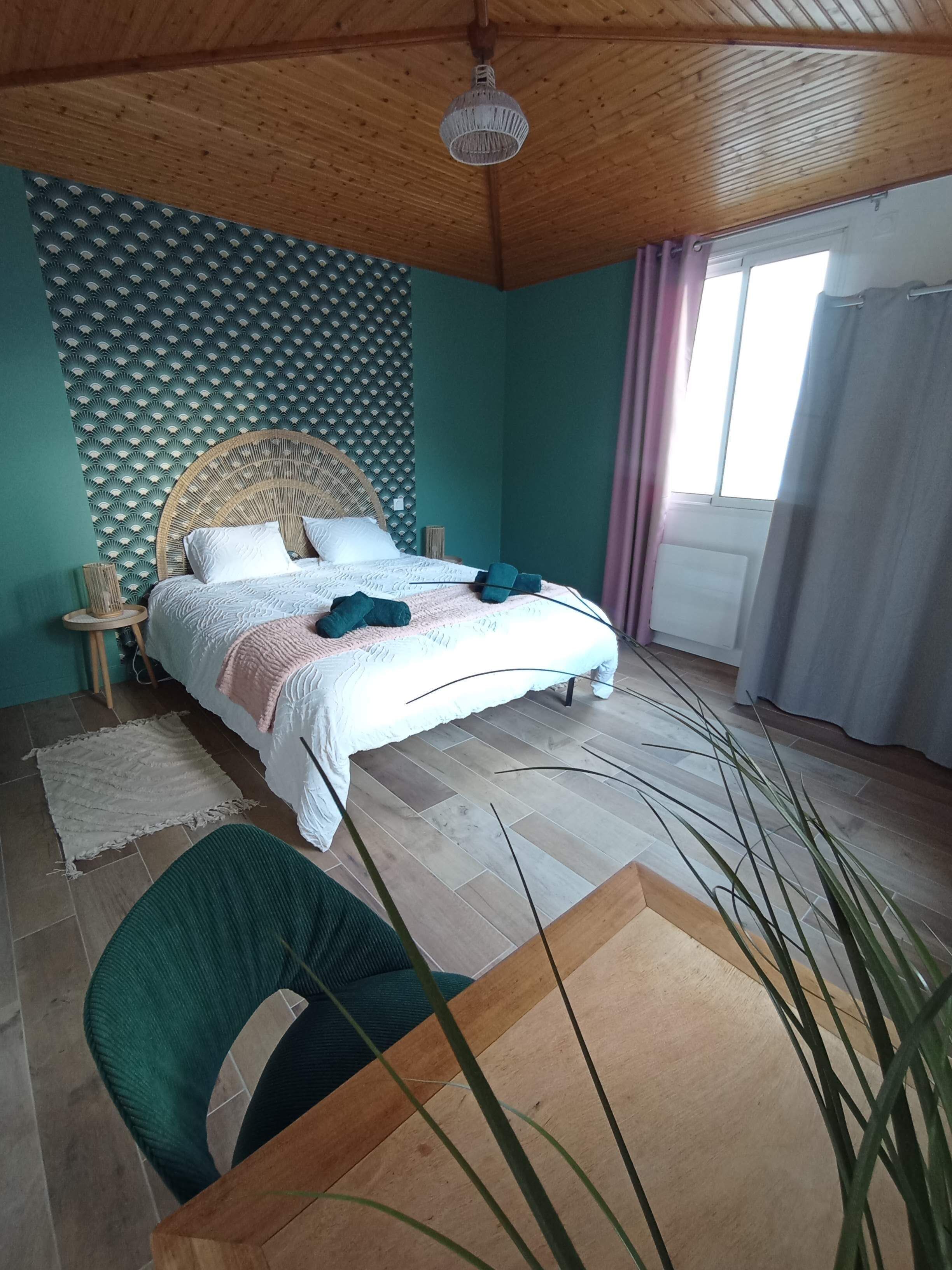 Een slaapkamer met een bed, een rond houten hoofdbord, een wandpaneel van geweven materiaal, een raam met gordijnen, een groene stoel en een houten vloer.