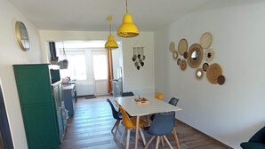 A dining area with a table, chairs, and hanging yellow pendant lights. - Gaby's Little House (Saint-Hilaire-de-Riez)