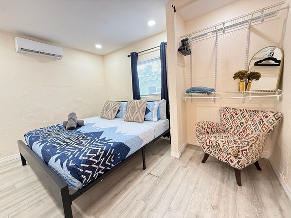 Quarto com cama, cadeira, prateleira suspensa e ar-condicionado fixado na parede.