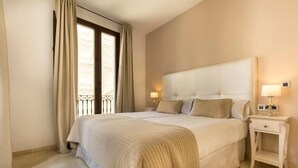 A hotel room with a large bed, two bedside lamps, a nightstand, and a window with curtains. - Siloe Plaza Apartments (Granada)