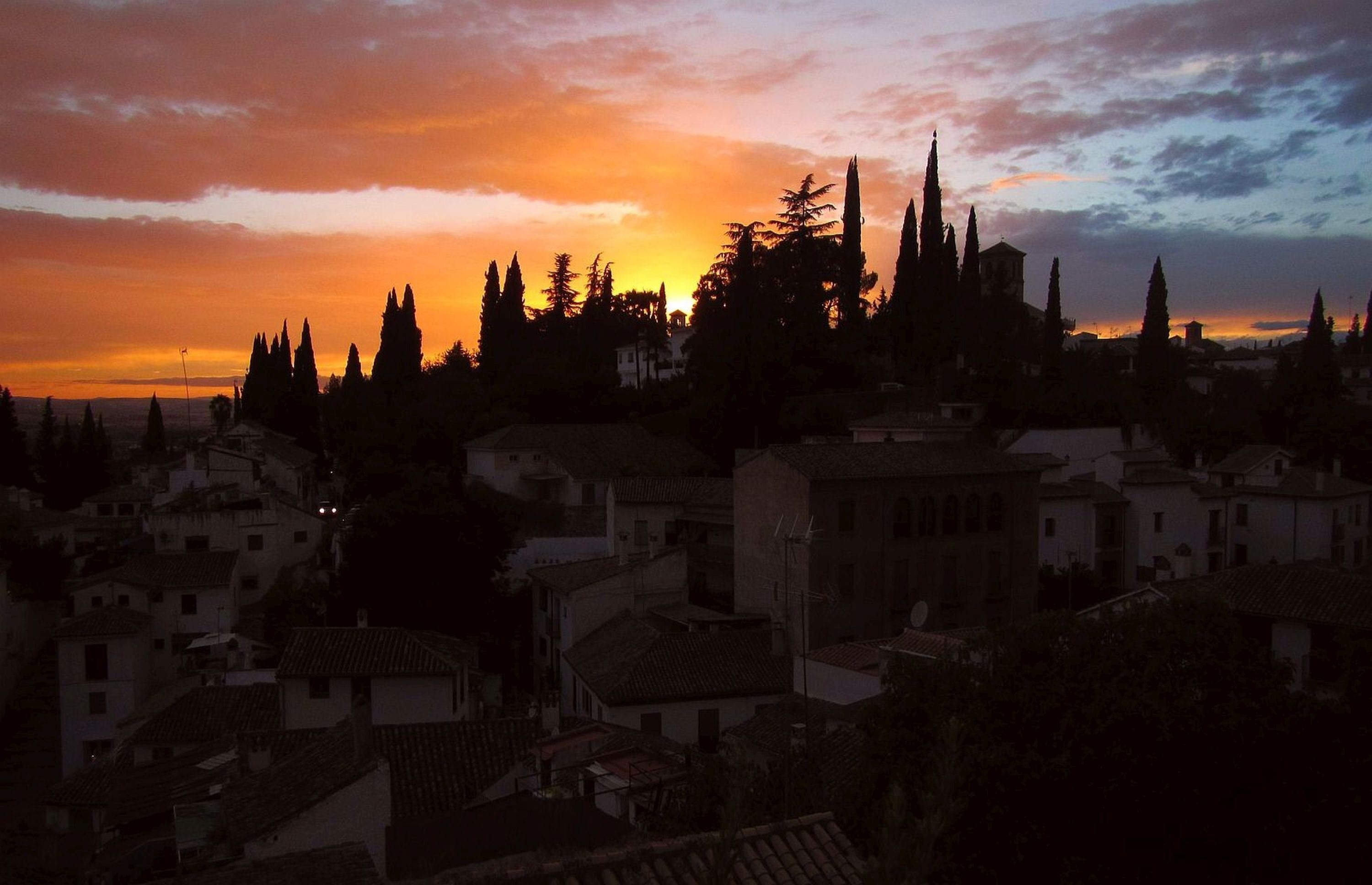 A town with buildings and trees silhouetted against a sunset sky.