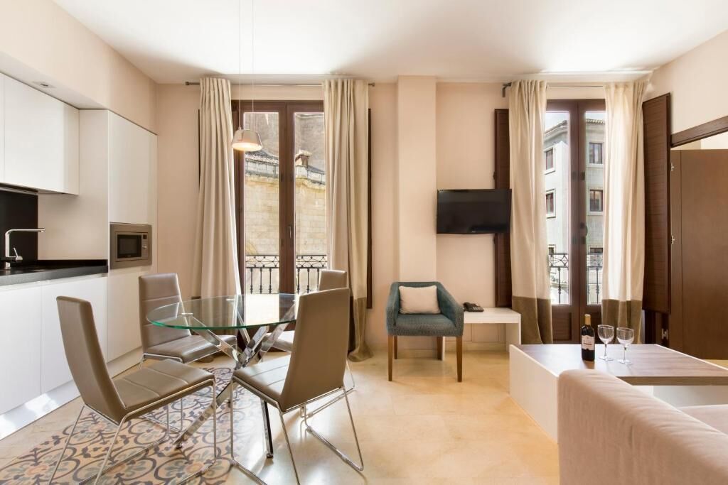 A modern hotel room with a dining area, a sofa, a TV, and a balcony with curtains.