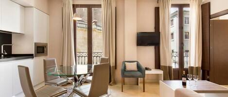Una habitación de hotel moderna con comedor, sofá, televisor y balcón con cortinas.