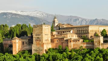 Un edificio histórico con una torre destacada, rodeado de exuberante vegetación y montañas al fondo.