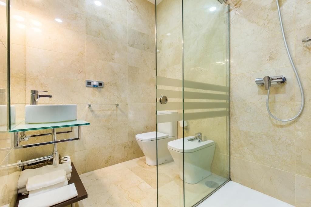 Een moderne badkamer met een douchecabine van glas, een glazen wastafel en een toilet.