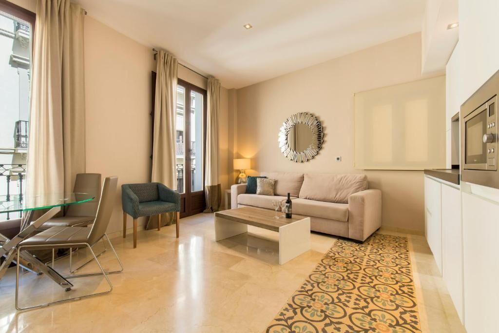 A modern living room with a glass dining table, a sofa, a coffee table, and a patterned rug.