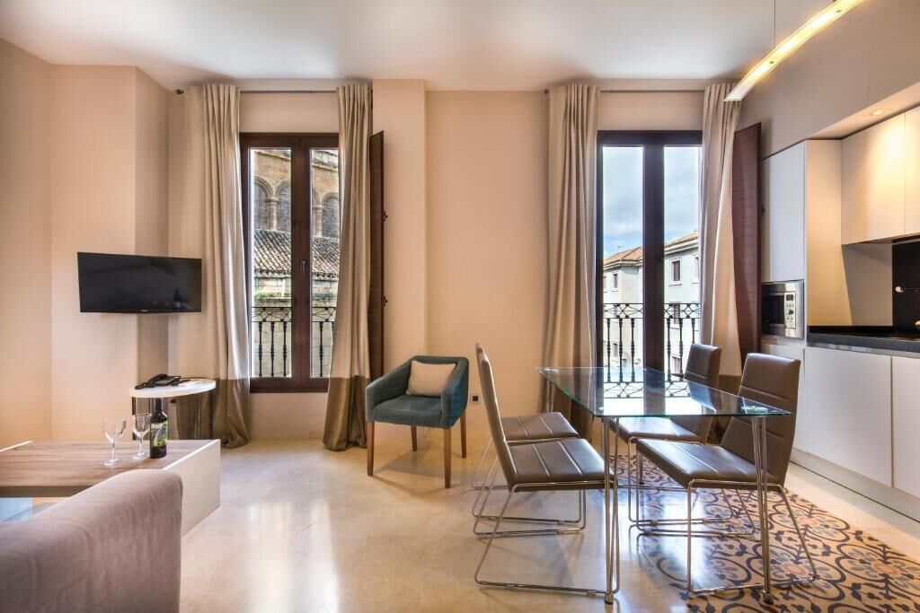 Een moderne hotelkamer met een glazen eettafel, een bank, een televisie en een keukenhoek.