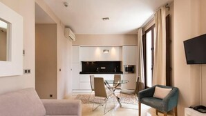 A modern living room with a sofa, a glass dining table, and a TV mounted on the wall. - Siloe Plaza Apartments (Granada)