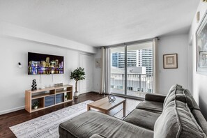 A modern living room with a large TV, a sofa, a coffee table, and a plant. - Brickell 2BR Escape | Stunning Water & City Views (Miami)