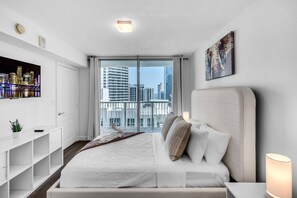 A modern hotel room with a large bed, a TV, a balcony with a city view, and a painting on the wall. - Brickell 2BR Escape | Stunning Water & City Views (Miami)