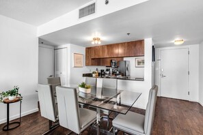 A modern kitchen with wooden cabinets, stainless steel appliances, and a glass dining table with chairs. - Brickell 2BR Escape | Stunning Water & City Views (Miami)