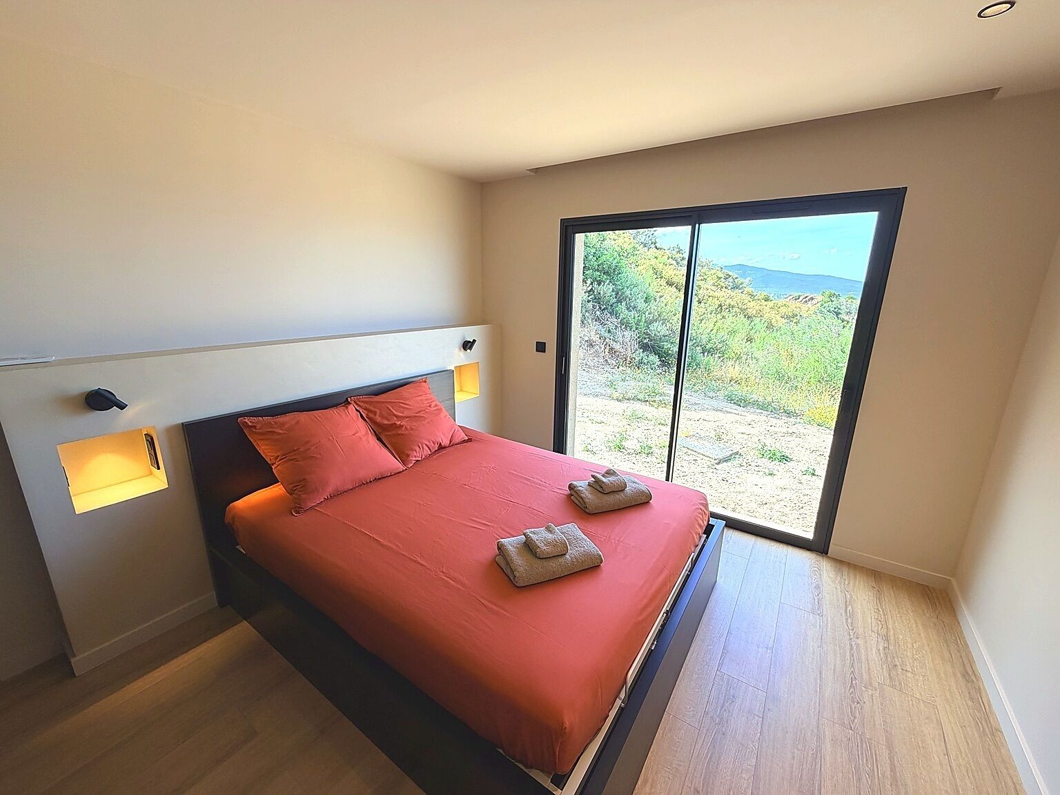 Une chambre à coucher avec un lit, une table de chevet, une fenêtre et une vue sur l’extérieur.