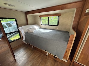 Ein kleines Schlafzimmer in einem Wohnmobil, mit einem Bett, einem Fenster und Blick auf geparkte Autos.