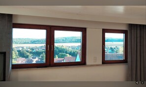 Ein Zimmer mit drei Fenstern und Blick auf eine ländliche Landschaft.
