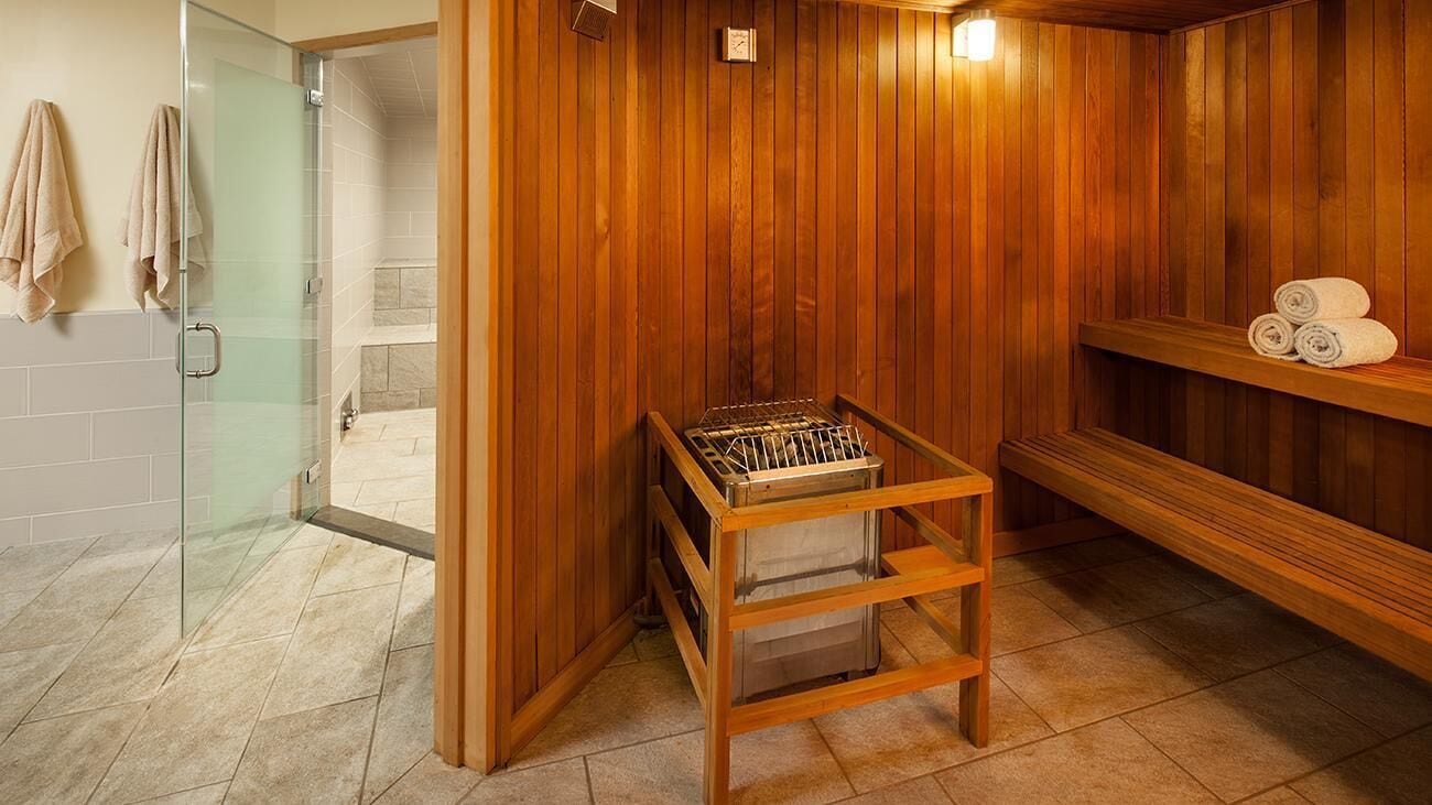 A sauna room with wooden walls, a glass door leading to a shower area, and a bench with towels.