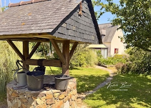 A rustic outdoor kitchen with stone walls and metal pots, set in a lush garden with a house in the background. - 4-bedroom house with a 7,000-square-meter garden, 950 meters from the sea (Plouézec)