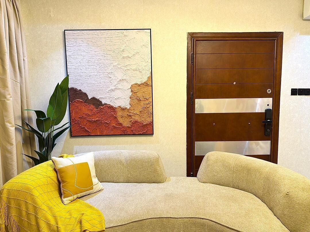 Une pièce avec un canapé beige, un plaid jaune, une grande plante verte et une porte en bois dotée d’un panneau de verre.
