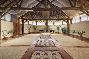 A spacious interior with a high wooden ceiling, a central fireplace, and multiple potted plants.