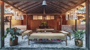Un área de estar al aire libre cubierta con un banco, mesas y decoraciones colgantes.