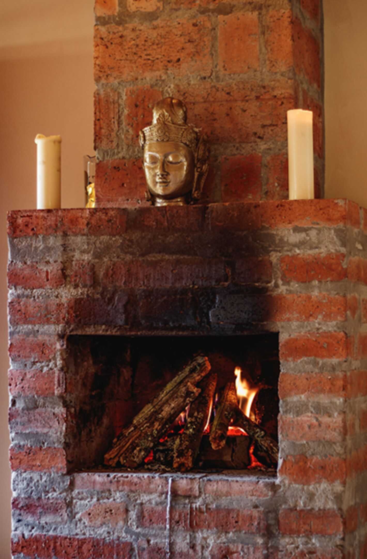A brick fireplace with a Buddha statue, two candles, and burning logs.