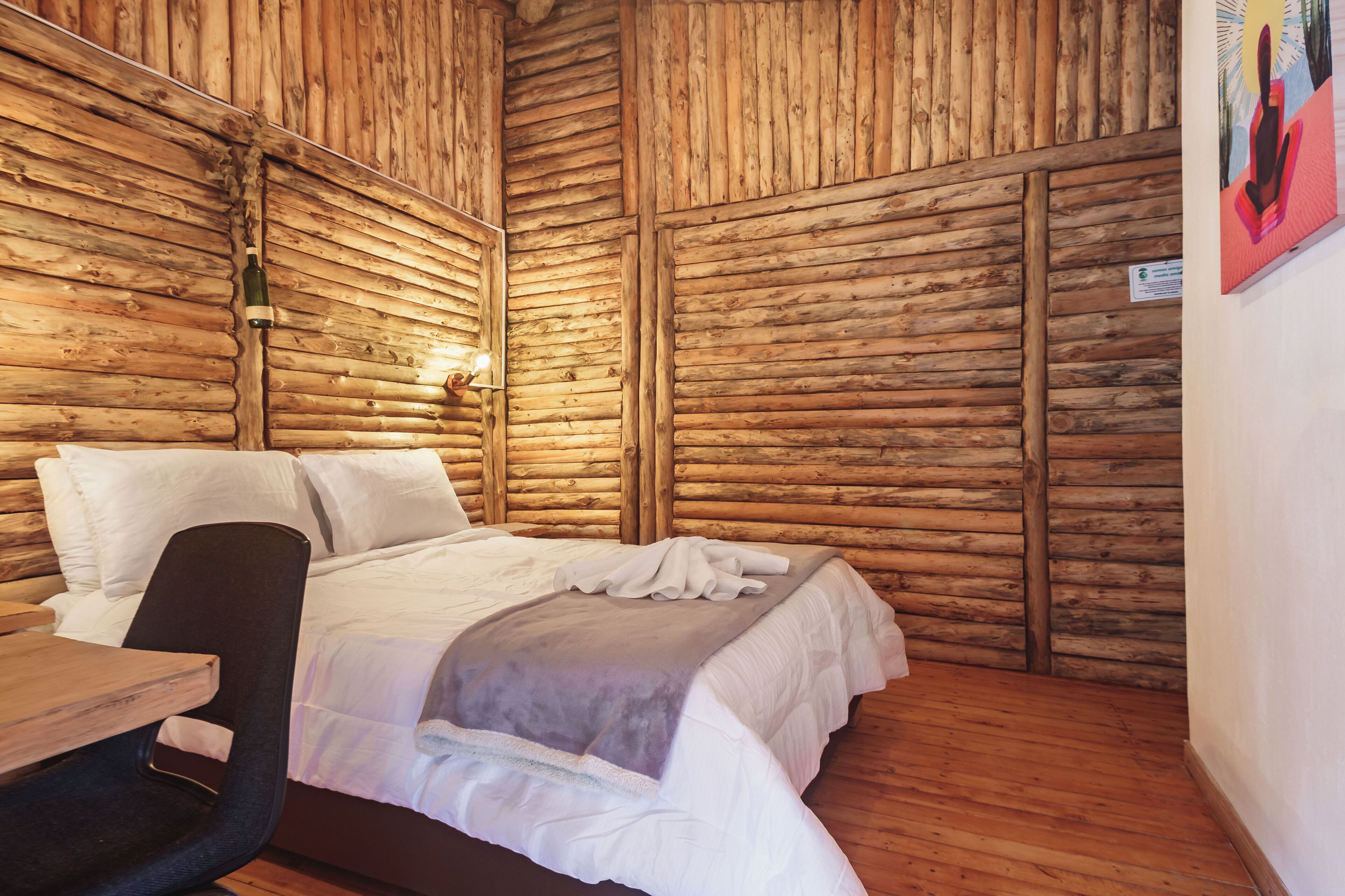 Una habitación tipo cabaña de madera con una cama, una silla y una mesa.