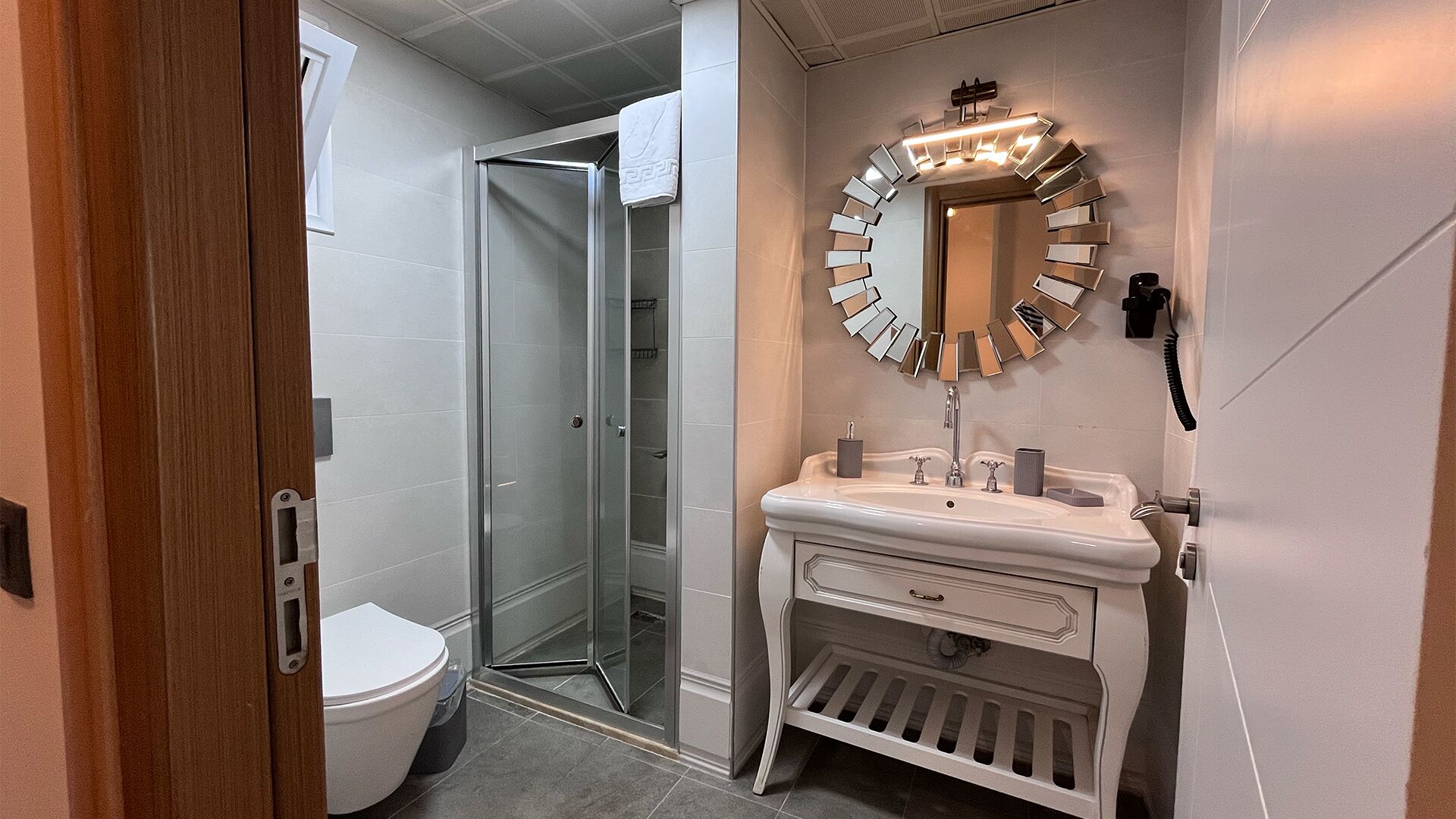 Ein Badezimmer mit Duschkabine aus Glas, einem weißen Waschbecken mit Spiegel und einer Toilette.