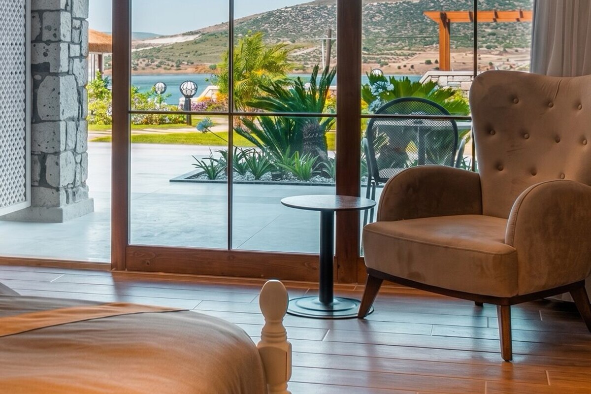A room with a large sliding glass door leading to a patio with a view of a hilly landscape and a body of water.