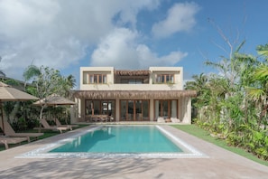 Un bâtiment à deux étages doté d’une piscine, de chaises longues et d’une végétation tropicale.