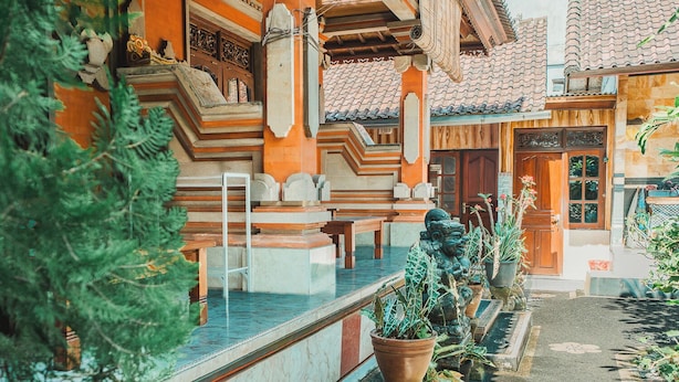 Un edificio tradicional con tejado de tejas, puerta de madera y un pequeño jardín con plantas en macetas.