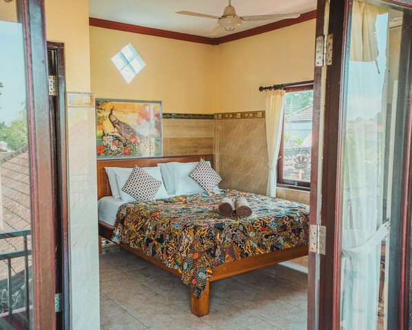 A bedroom with a bed, a ceiling fan, a window with curtains, and a wall with a decorative piece.