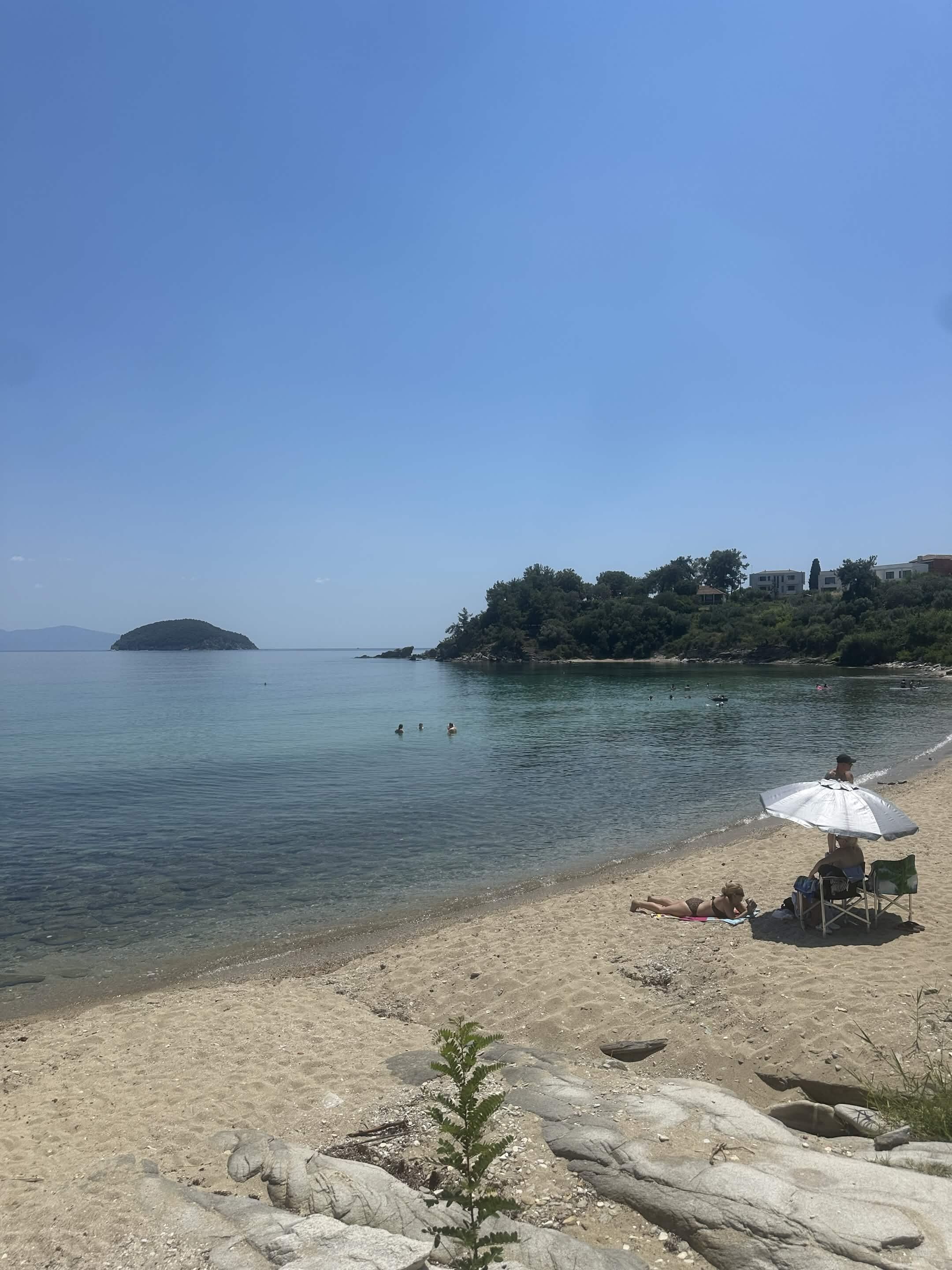 Une plage à l’eau claire, une petite île qui se dessine à l’horizon et quelques personnes qui se baignent.