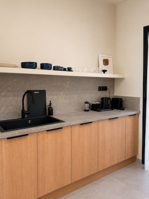 Eine moderne Küche mit schwarzem Spülbecken, Holzschränken und einer Marmorarbeitsplatte, inklusive Kaffeemaschine.