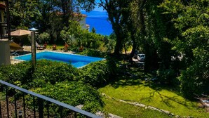 Una piscina circondata da vegetazione lussureggiante, cielo azzurro limpido e vista sul mare.