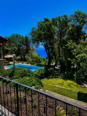 Ein Pool, umgeben von üppiger Vegetation, einem strahlend blauen Himmel und Blick auf das Meer.