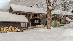 Ein rustikales Holzhäuschen mit schneebedecktem Dach, einem Holzzaun und einem Holzstoß.