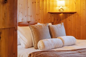 Ett rum med träpanel på väggarna, en säng, två kuddar, en filt och en vägglampa.