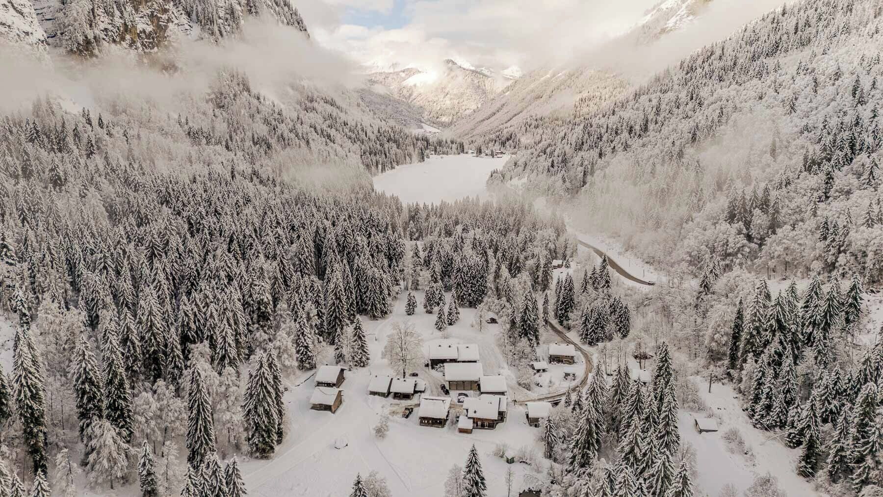 Bosque nevado con un lago y varias cabañas.