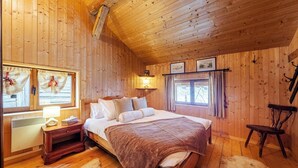 Ein gemütliches Schlafzimmer einer Holzhütte mit Bett, Nachttisch, Lampe und einem Fenster mit Vorhängen.