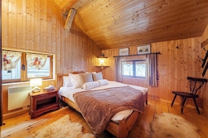 Ein gemütliches Schlafzimmer einer Holzhütte mit Bett, Nachttisch, Lampe und einem Fenster mit Vorhängen.