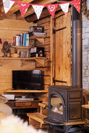 Ein gemütliches Blockhaus-Interieur mit Kaminofen, Bücherregalen und einem Fernseher.