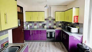 Una cocina compacta con gabinetes morados y amarillos, un salpicadero de azulejos y una campana extractora de acero inoxidable.