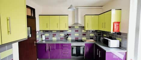 Una cocina compacta con gabinetes morados y amarillos, un salpicadero de azulejos y una campana extractora de acero inoxidable.