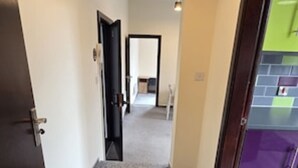 Un pasillo con piso alfombrado que conduce a una habitación con pared morada y puerta verde.